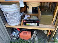 Shelf with white buckets, box of collated fencing nails, metal toolbox, orange/red gas can, jack stand, and collated fencing staples box.