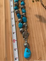 Close-up photo showing turquoise and silver beads, decorative toggle clasp, and pendant with a measuring tape for scale.