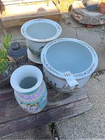 Photo showing all three porcelain pots consisting of two large open pots and one tall decorative vase, positioned on wooden surface outdoors.