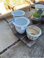 Photo shows three vintage Chinese porcelain pots arranged on outdoor table. Two pots have decorative borders near rim; one pot depicts a dragon motif in relief with colored glaze. Light and shadows indicate outdoor daytime setting.