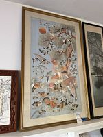 Framed vintage Chinese hand stitched silk wall art featuring various birds, tree branches, and a sun in the background, hung on a wall.