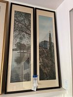 Two vertically framed art pieces hanging on a wall showing Asian landscape scenes: tree over lake and pagoda tower on rocky hill.