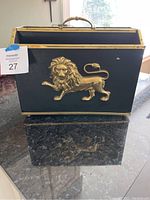 Front view of black magazine rack featuring a brass lion figure and brass edges on a dark marble surface