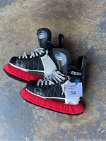 Side view of CCM Powerline 120 Hickey hockey skates with red blade covers on scuffed concrete floor.