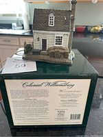 Front view of ceramic Shoemaker Shop with chimney and stone wall on original box showing product and brand information.