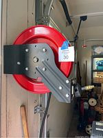 Side view of red spring loaded hose reel mounted on wall, with black compressor hose and metal mounting bracket visible.