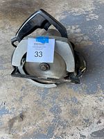 Top and side view of electric handheld circular saw showing blade and handle.