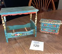 Full view of painted wood doll canopy bed and matching dresser set on wooden table showing scale and style.