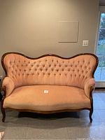 Front view of French camelback sofa showing peach tufted upholstery and wooden frame details.