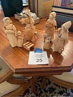 Set of six handmade corn husk figures on wooden table with books in background, showing grouping and relative size