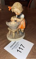 Front angled view of the W Goebel Hummel figurine showing girl washing baby doll in basin, highlighting painted details and overall condition.
