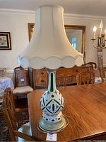 Full view of the lamp on a wooden table showing the lampshade and base with floral and green glass details