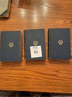 Top down view of three blue hardcover books with gold embossed emblem on front covers.