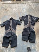 Two adult small black wetsuits with front zippers, short sleeves, and short legs, laid out on a worn surface