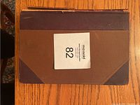 Top view of the hardcover book showing brown cloth covers with dark brown leather corners and edges with some wear.