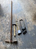 Hoe, claw hammer, and two hacksaws laid out on the ground showing all items in lot