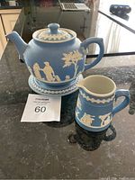 Front view of tea pot with lid and matching creamer, all in blue jasperware style with white relief decoration on black countertop.