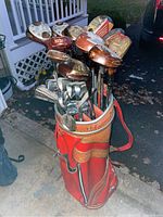 Full view of golf clubs in red leather golf bag showing wood and iron clubs.