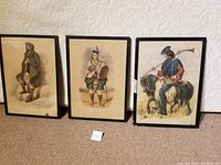 Three framed lithographs displayed upright on floor, showing full figures of clansmen.