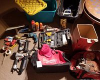 First photo showing contents of the two plastic bins including various tools and accessories spread out on floor near two tool bags and an empty box