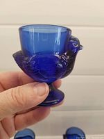Close-up of one cobalt blue glass hen-shaped egg cup, showing detailed hen form and thick glass egg holder