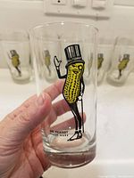 Close-up photo showing clear glass tumbler held in hand, with Mr. Peanut print in black, yellow, and white.