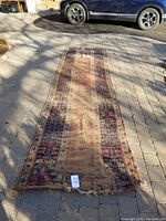 Wide shot of the full length of the antique hallway runner rug laid out on a paved surface showing discoloration and wear