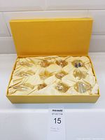 Yellow satin-lined box containing 12 glass suncatchers arranged in 4 groups of 3, each in individual compartments, packed and unused.