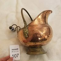 Full view showing the shape of the copper coal scuttle with handle and pedestal base.