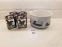 Photo showing the set of four glass tumblers with loon bird designs and one white ceramic bowl with black loon illustrations on a flat surface.