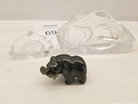 Three small miniature carvings placed next to each other: a dark jade bear holding a salmon, a clear glass Mats Johanson seal, and a glass loon carving.
