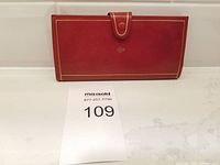 Front view of red leather wallet with snap closure and gold stitching laying on white surface.