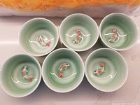 Six ceramic tea cups showing the raised koi fish motif inside each one, glazed in celadon green.