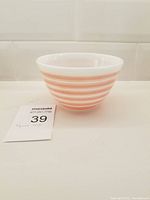 Side view of small white Pyrex bowl with horizontal pink stripes and lot number card beside it.