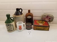Photo of entire lot showing pottery bottles, amber glass bottle, Glasbake mug, and antique tins arranged on surface.