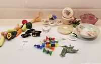 Full overview of lot contents showing diverse trinkets arranged on white surface including ceramics, glass candy figurines, black lacquer bunny dishes, and a marble candle holder.