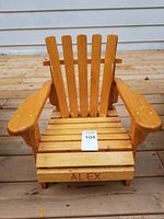 Front view of the wooden toddler Adirondack Muskoka style deck chair showing the name 'Alex' painted on the front slat of the seat. Chair is on a wooden deck surface.