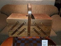 Closed view of the vintage wood sewing box showing the handle and accordion structure on the sides.