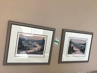 Two framed limited edition prints displayed on the wall side by side, showcasing scenic landscapes with water and houses.