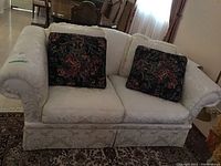 Front view of the upholstered Barrymore couch with cream damask fabric and two floral cushions.