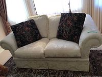 Full view of Barrymore upholstered couch with two white seat cushions, two white back cushions, and two black floral decorative cushions on each side.