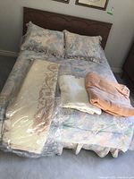 Photo of double size wooden bed with scalloped headboard and floral bedding with pillows, two blankets, one bedcover on top.