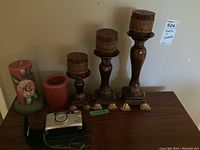 Photo showing five candles and holders, Nikon One Touch Zoom 90s camera with case on a shelf against a beige wall.