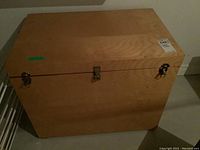 Top and front view of a rectangular wooden chest with metal latches and handles. The chest is made of light-colored wood with visible grain and natural finish.