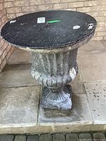 Front view of the cement planter showing the urn shape and wear on the surface with black removable top.