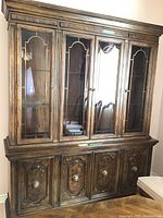 Front view of two-piece china cabinet showing four glass doors on upper section and four wooden doors below.