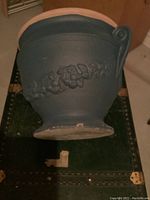 Blue clay planter pot viewed from the side showing the decorative raised vine and grape motif and unpainted rim.