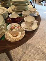 Five cups and matching saucers with varied bone china patterns and colors on a wooden table.