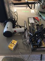 Table with white and black hairdryer, three curling irons, and yellow/white electricity converter box.