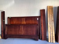 Photo showing the headboard, footboard, and side rails of the mahogany finish king sleigh bed frame leaning against a wall.